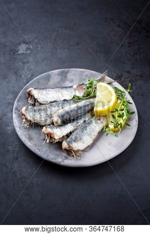 Fried sardines with lrmon slices and herbs offered as closeup on a modern design plate with copy space