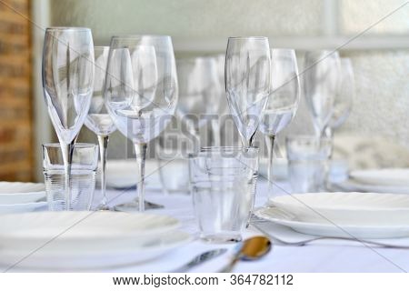Close Up New Diverse Of Glassware And Porcelain Plates Served On White Tablecloth, No People. Table 