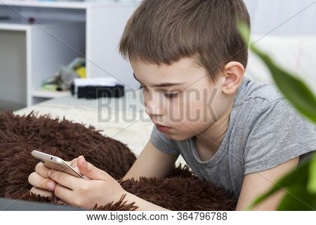 A Boy Of 8-9 Years Old Is Lying On The Bed With A Phone. Home Schooling. Quarantine Coronavirus Isol