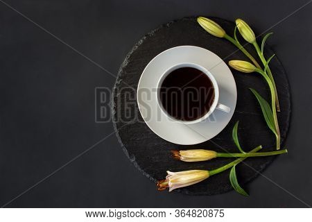 Cup Of Black Coffee Tea And Fresh Spring Buds Of Lily Flowers On A Round Slate On A Black Background
