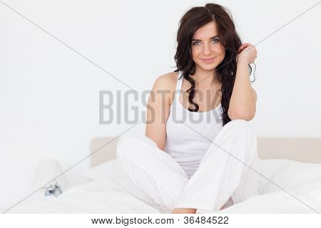 Smilende brunette kvinde sidder på hendes seng med benene krydsede indendørs