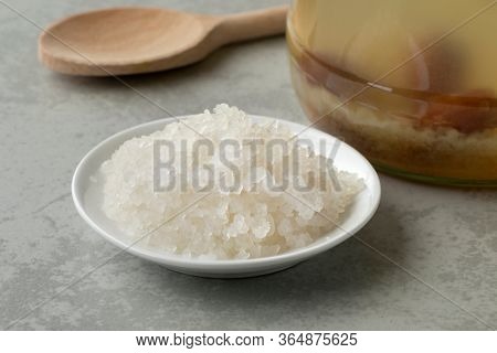 Bowl with organic probiotic water kefir grains in front of a glass jar filled with grains and fruit