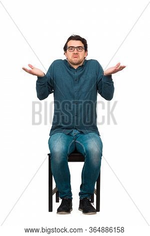 Full Length Of Doubtful Businessman, Keeps Hands Outstretched, Shrugging Shoulders Gesture, Sitting 