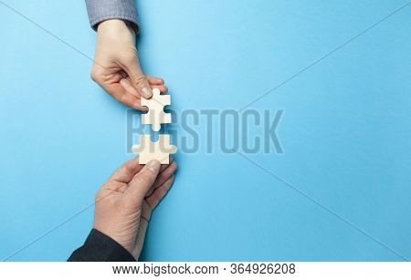 Two Hands Connect Puzzles On A Blue Background. Cooperation And Teamwork In Business. Collaboration 