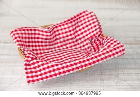 Wicker Basket With A Red Checked Fabric Napkin On A Wooden White Table
