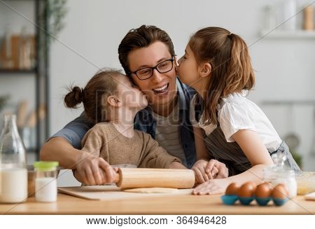 Happy loving family are preparing bakery together. Father and children daughters girls are cooking cookies and having fun in the kitchen. Homemade food and little helper.   