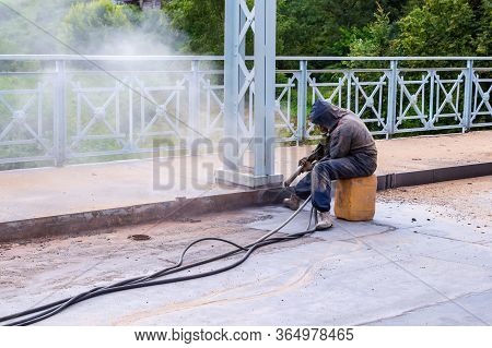 Worker With Protective Mask Works A Bridge With Sandblast. The Sandblasting Process