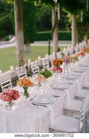Wedding Dinner Table Reception. A Very Long Table For Guests With A White Tablecloth, Floral Arrange