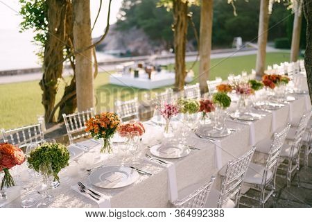 Wedding Dinner Table Reception. A Very Long Table For Guests With A White Tablecloth, Floral Arrange