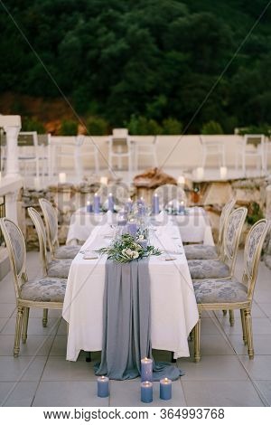 Wedding Dinner Table Reception. A White T-shaped Table With A Grey Tablecloth And Lots Of Blue Candl