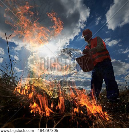 Fireman Ecologist Fighting Fire In Field With Cloudy Sky On Background. Male Environmentalist Holdin