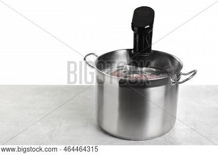 Sous Vide Cooker And Vacuum Packed Food Products In Pot On Light Marble Table Against White Backgrou