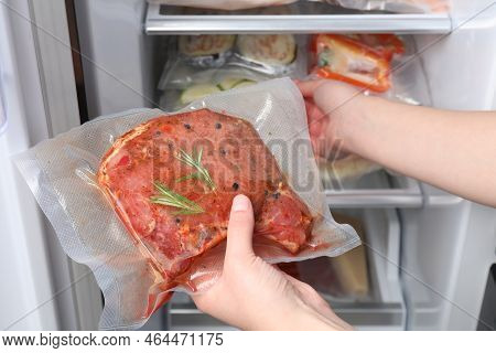 Woman Putting Vacuum Bag With Meat Into Fridge, Closeup. Food Storage