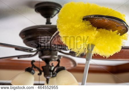 Using A Wand Feather Duster To Remove And Clean Dust From A Ceiling Fan