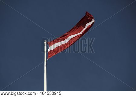 Waving National Flag Of Latvia On The Background Of Dark Blue Sky.