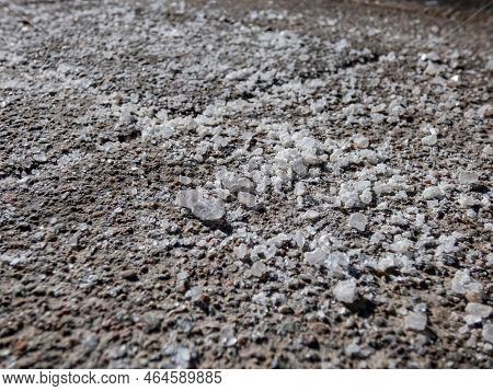 Macro Shot Of Big, White Salt Grains On Icy Sidewalk Surface In The Winter In Sunlight. Applying Sal