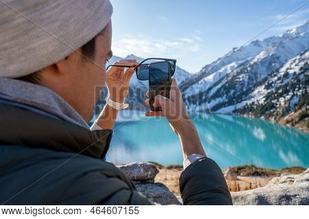 Over The Shoulder Image Of A Warmly Dressed Man Taking A Picture With His Phone Through Polaroid Sun