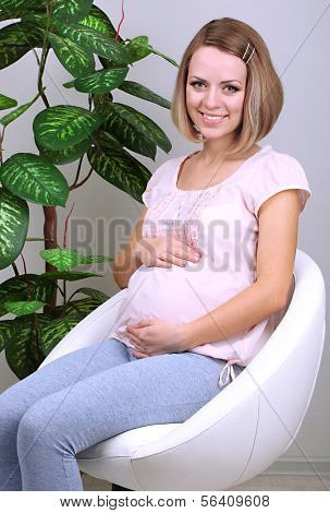 Young regnant woman sitting on armchair at home