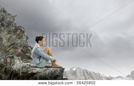 Image of young upset businesswoman sitting alone atop of mountain