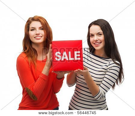 shopping, sale, and gift sconcept - two smiling teenage girls with sale sign on red box