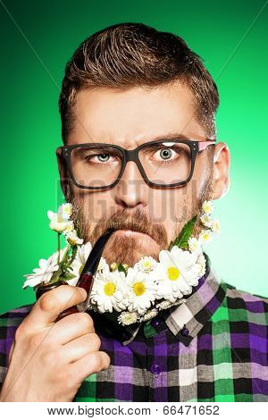 Handsome young man in glasses and a beard of flowers smoking a pipe. 