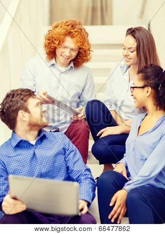 business, technology and startup concept - smiling creative team with laptop and tablet pc computer sitting on staircase