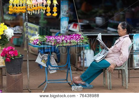 THONG PHA PHUM, THAILAND, JULY 07, 2012: A street flower woman seller is sitting and reading a newspaper in the village of Thong Pha Phum in the Kanchanaburi province, Thailand