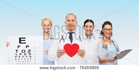 medicine, profession, teamwork and healthcare concept - international group of smiling medics or doctors with clipboard and stethoscopes holding red paper heart shape over blue background