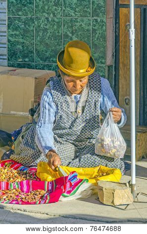 COPACABANA, BOLIVIA, MAY 6, 2014: Local woman in traditional costume and bowler hat sells grilled bean on street