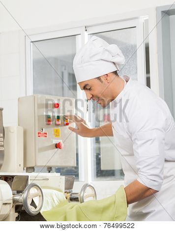 Side view of male chef operating spaghetti pasta machine at commercial kitchen