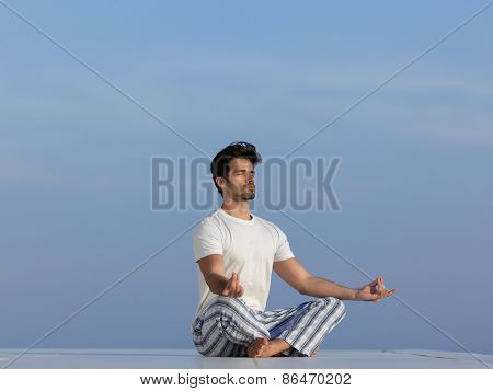 handsome young man practicing yoga on in modern home terace with ocean and sunset in background