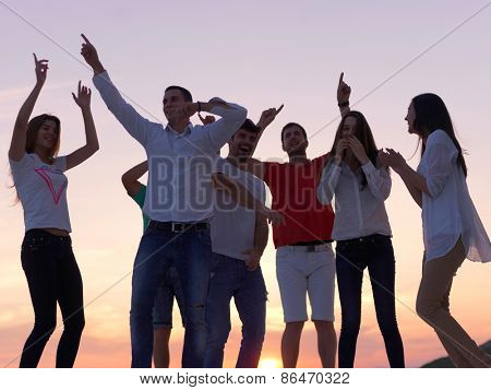 group of happy young people dancing and have fun on party in modern home bacony with sunset and ocean in background