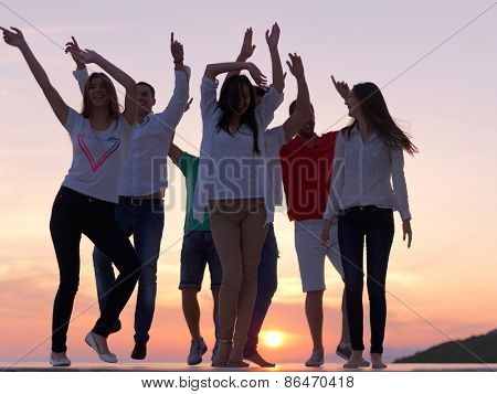 group of happy young people dancing and have fun on party in modern home bacony with sunset and ocean in background