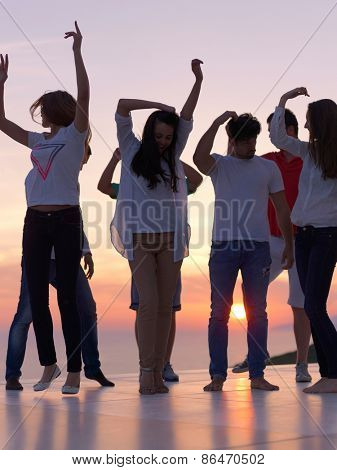 group of happy young people dancing and have fun on party in modern home bacony with sunset and ocean in background