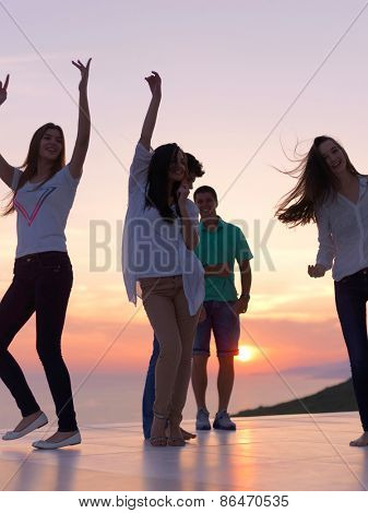 group of happy young people dancing and have fun on party in modern home bacony with sunset and ocean in background