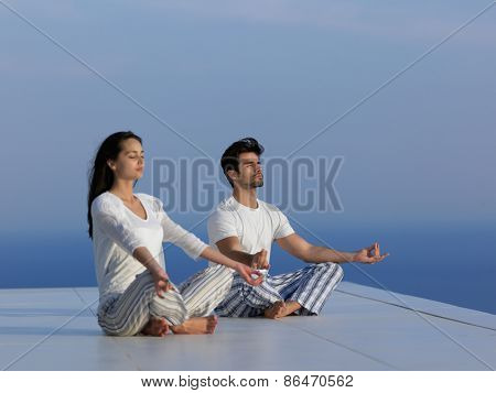 young couple practicing yoga at sunset in modern home terace with ocean and sunset in background