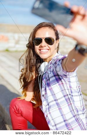 holidays and tourism concept - smiling teenage girl taking picture with smartphone camera aoutdoors