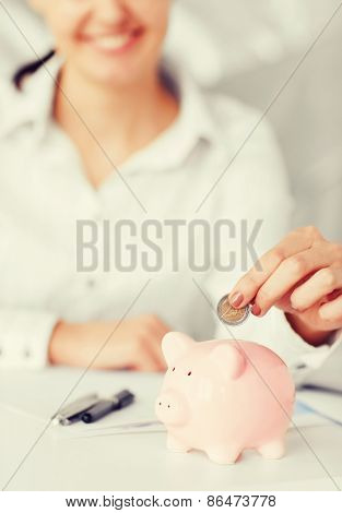 business, office, household, school, tax and education concept - woman hand putting coin into small piggy bank