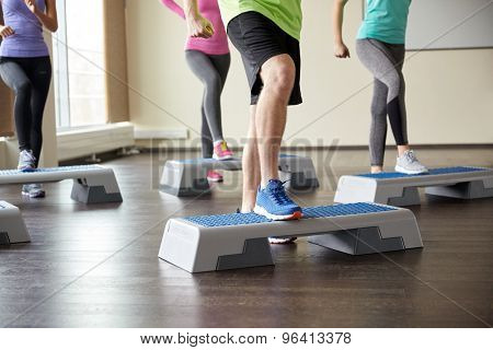 fitness, sport, aerobics and people concept - group of smiling people working out and flexing legs on step platforms in gym