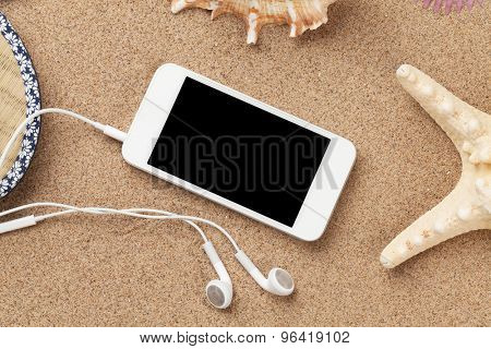 Smartphone on sea sand with starfish and shells. Top view with copy space