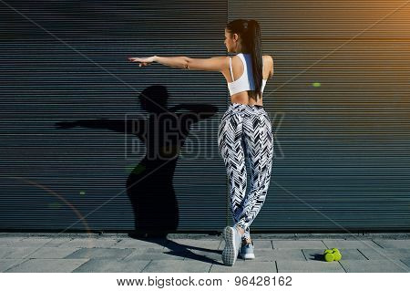 Young woman with perfect figure stretching her hands against black wall with copy space