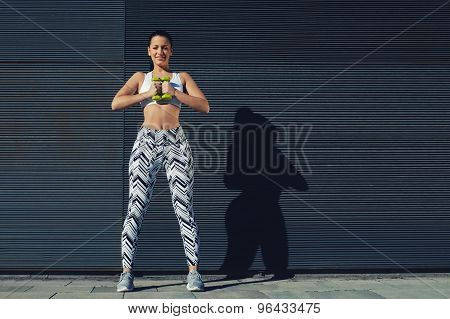 Young woman in sporty clothing training bicep curls outdoors with copy space background