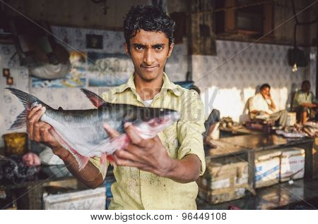 MUMBAI, INDIA - 08 JANUARY 2015: Worker on a fishmarket next to Dhobi ghat shows fish while waiting for customers. Post-processed with grain, texture and colour effect.