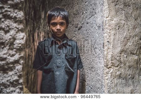 MUMBAI, INDIA - 12 JANUARY 2015: Young Indian boy from Dharavi slum stands in empty narrow street. Post-processed with grain, texture and colour effect.