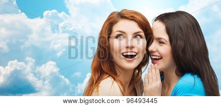 friendship, secrecy and people concept - two smiling girls or young women whispering gossip over blue sky with clouds background
