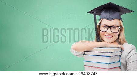 education, high school, knowledge, and people concept - picture of happy student girl or woman in trencher cap with stack of books over green chalk board background