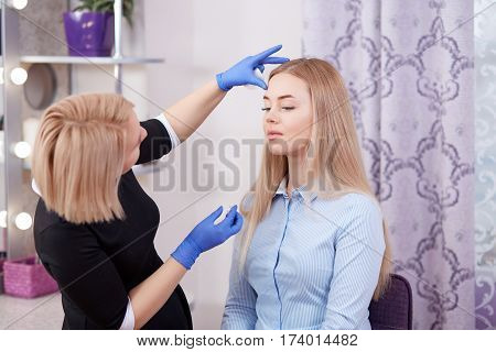 Side view of cosmetologist in black dress cleaning face her client in beauty salon looking from distanse by results. Makeup artist touching face of clent after procedure of cleaning and makeup.
