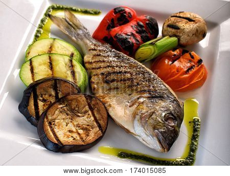 Dorado fish on a white plate with vegetables grill
