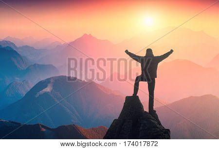 Hiker standing on a peak of mountain with raised hands and rejoices sunrise above the misty valley.