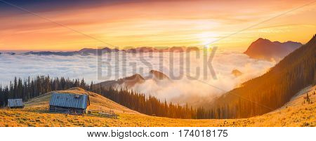 Sunrise above the high montain foggy valley with old wooden houses on a hill.